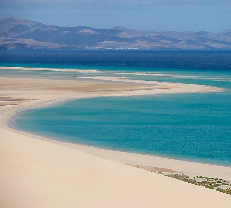 Playa de arena blanca y agua turquesa, vista de monta&ntilde;as al fondo