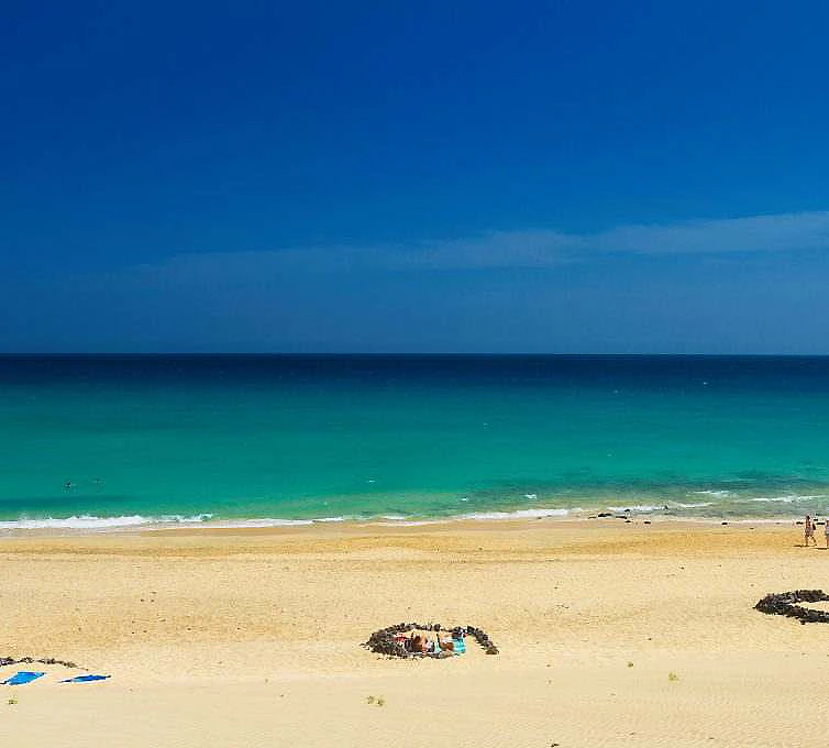 Playa de arena dorada con mar turquesa y cielo azul despejado.