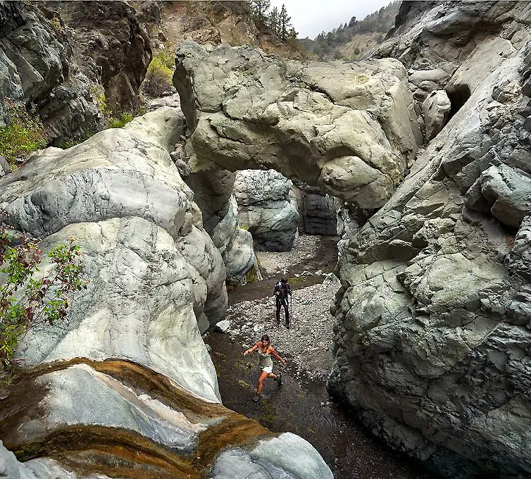 Sendero entre rocas en un ca&ntilde;&oacute;n monta&ntilde;oso con dos excursionistas al fondo.