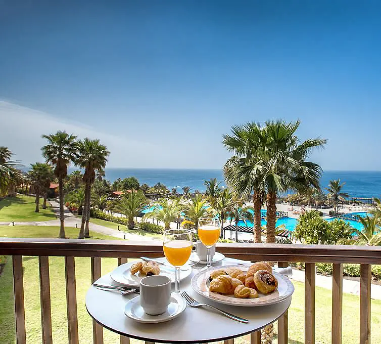 Desayuno en balc&oacute;n con jugo, croissants y vista al mar y palmeras