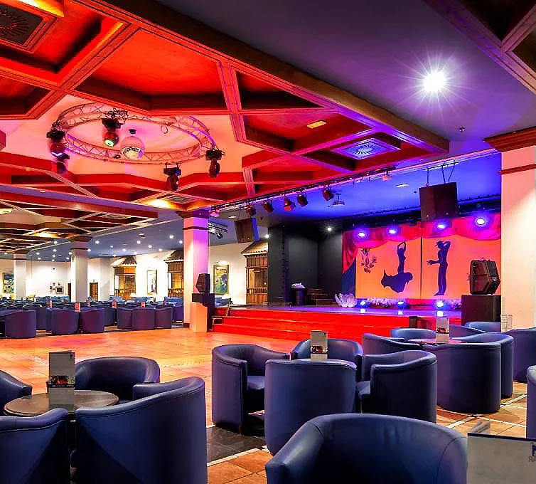 Sal&oacute;n con sillones y escenario iluminado con luces moradas y rojas