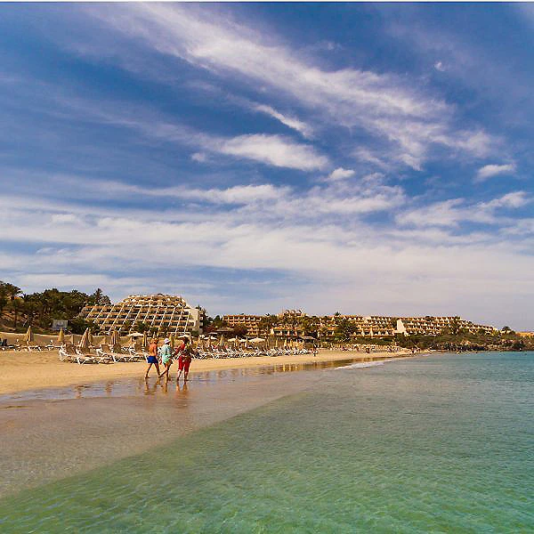 Playa con hotel frente al mar y dos personas caminando por la orilla