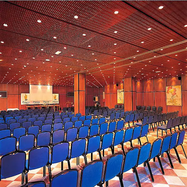 Sala de teatro con filas de butacas azules y techo rojo con luces.