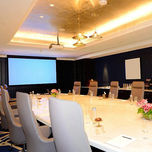 Sala de conferencias con mesas decoradas, luces y proyector en pared.