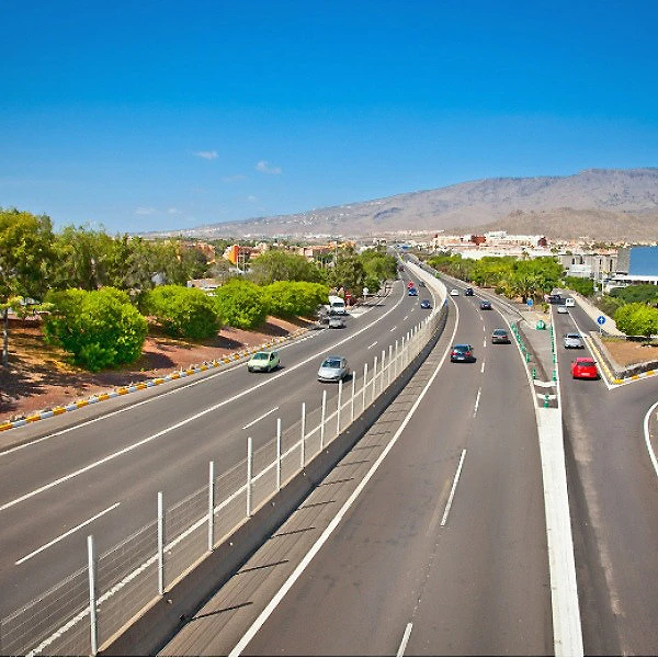 Autopista con tr&aacute;fico y paisaje costero bajo cielo azul y monta&ntilde;as.