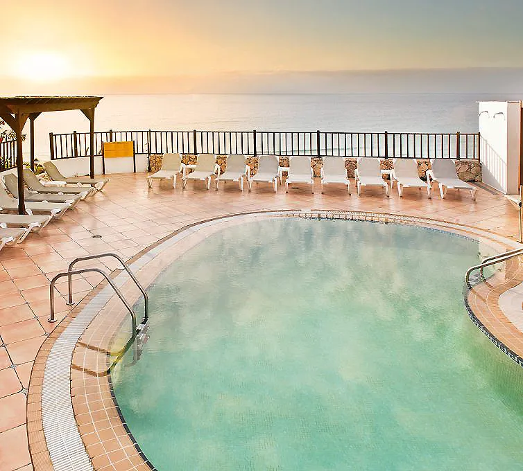 Piscina climatizada al atardecer con tumbonas y vista al mar, terraza.