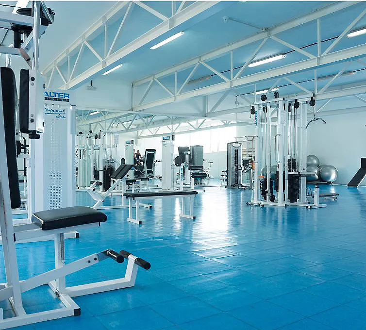 Gimnasio moderno con m&aacute;quinas de pesas y bancos, luces y piso azul