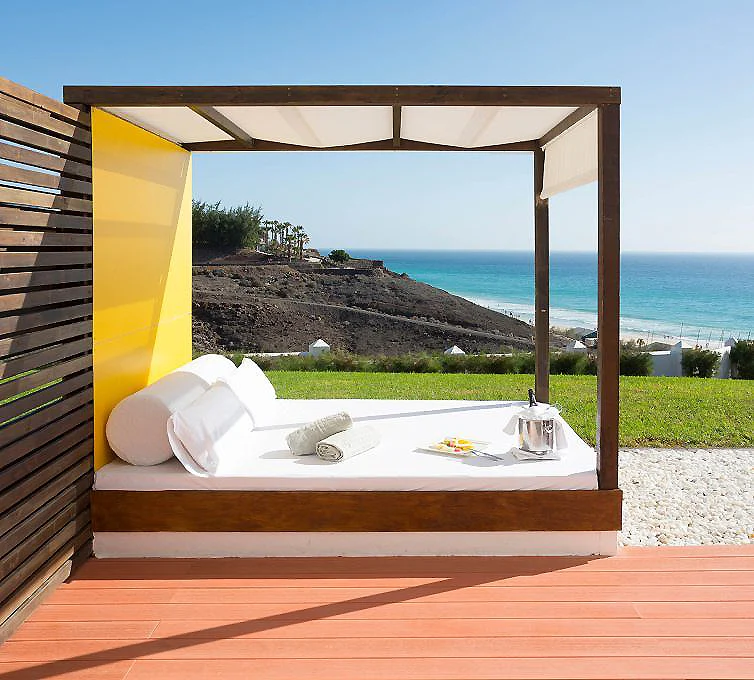 Cama balinesa bajo p&eacute;rgola con vista al mar y jard&iacute;n junto a la costa.