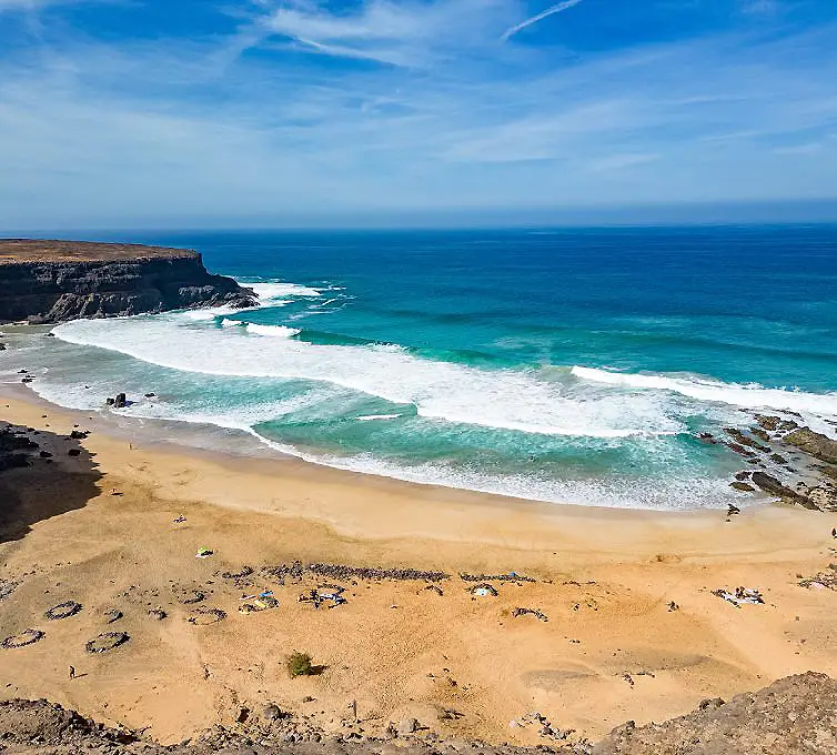 Playa de arena dorada con olas rompiendo y acantilados bajo cielo despejado