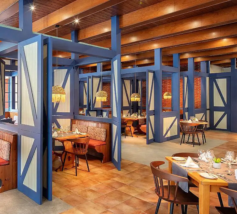 Interior de restaurante con mesas, sillas de madera y paneles azules y blancos.