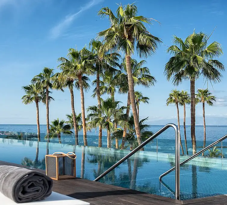 Piscina junto al mar con palmeras y toalla enrollada sobre el borde