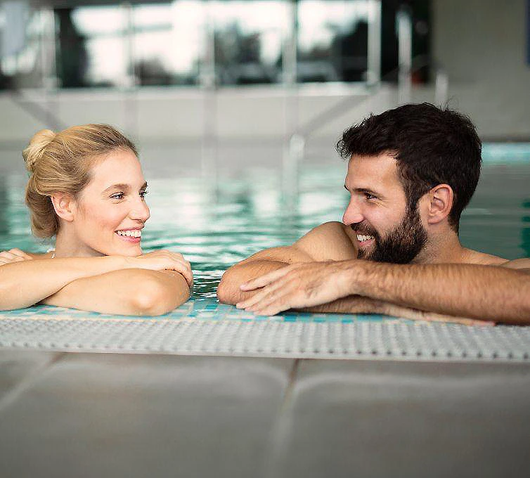 Pareja sonriente en una piscina cubierta, apoyados en el borde