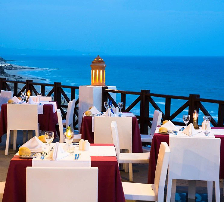Mesa con manteles blancos y vista al mar desde un muelle, con faro al fondo.