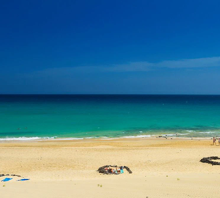 Playa de arena dorada con olas turquesa y cielo azul despejado