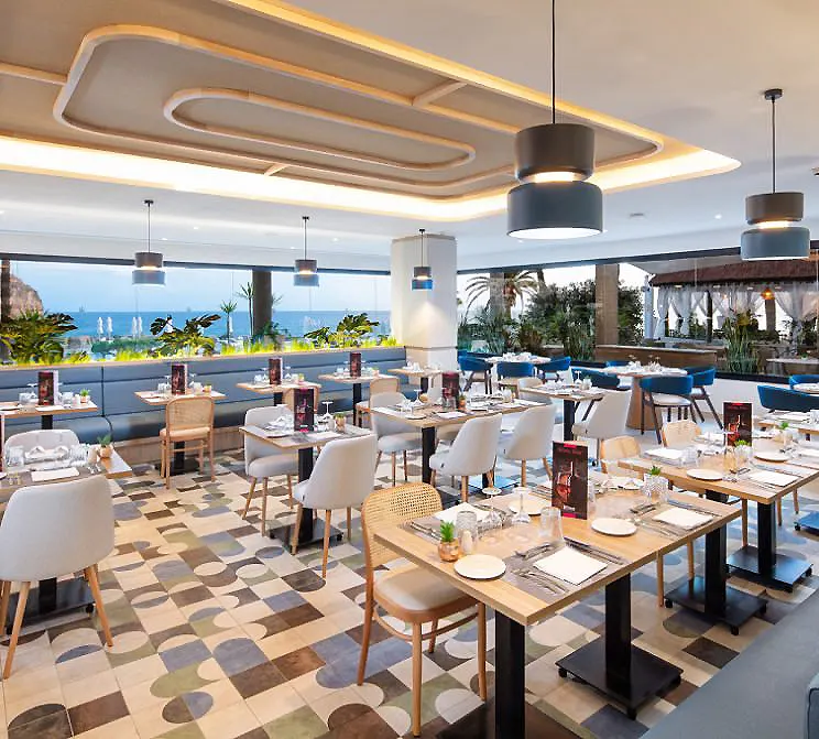 Restaurante con mesas y sillas bajo luz colgante y vista al mar.