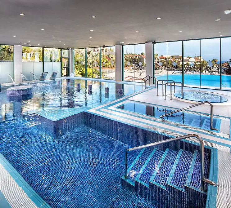 Piscina interior climatizada con chorros y tumbonas, vista al mar.