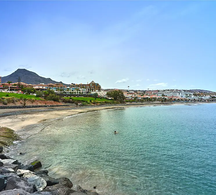 Playa costera con casas y monta&ntilde;as al fondo, aguas turquesa.