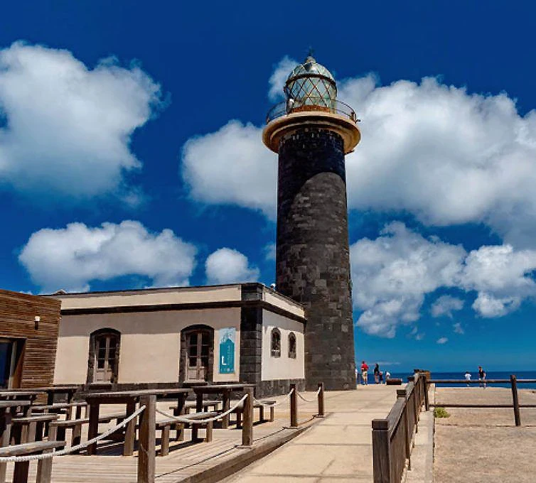 Faro de piedra y blanco junto al mar, con cielo azul y nubes
