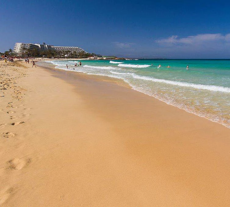 Playa de arena dorada con mar turquesa y ba&ntilde;istas bajo cielo despejado