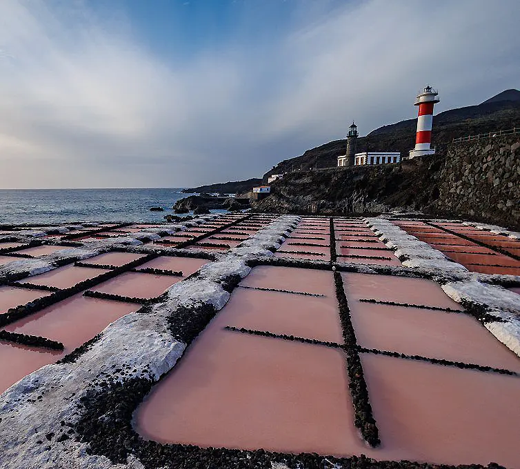 Camino de sal con piscinas rosadas y faro rojo junto al mar