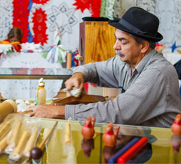 Artesano con sombrero trabaja con piezas de madera en un taller decorado.