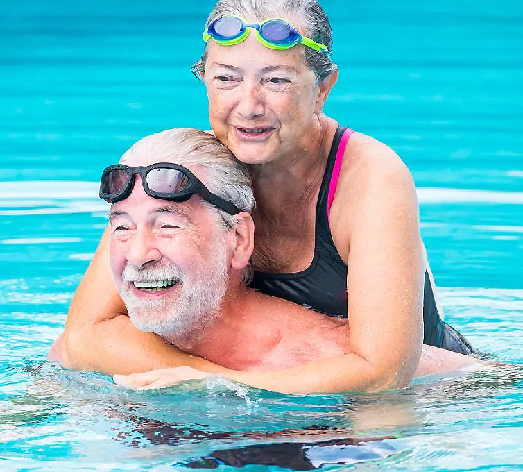 Mujer mayor con gafas en la piscina abraza a un hombre con m&aacute;scara de buceo