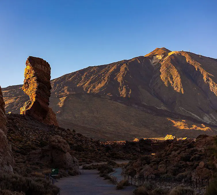 Monta&ntilde;as doradas al atardecer con un camino entre arbustos y rocas.