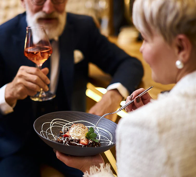 Cena en restaurante: mujer sirve un plato mientras un hombre brinda con vino