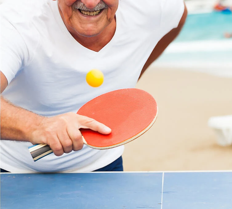 Hombre juega ping-pong, golpeando la pelota con una raqueta roja.