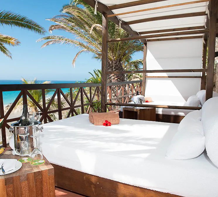 Cama blanca con dosel y vista al mar entre palmeras, en terraza.