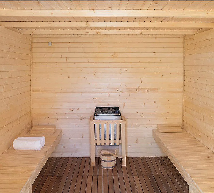 Interior de sauna de madera con cubo, toallas y hornillo en el centro