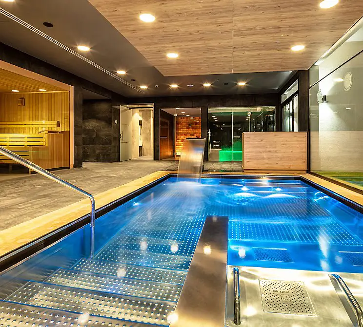 Piscina interior con techo de madera, luces LED y zona de sauna.