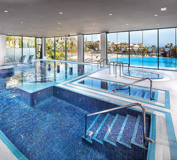Piscina cubierta con jacuzzi y grandes ventanales hacia la alberca exterior.