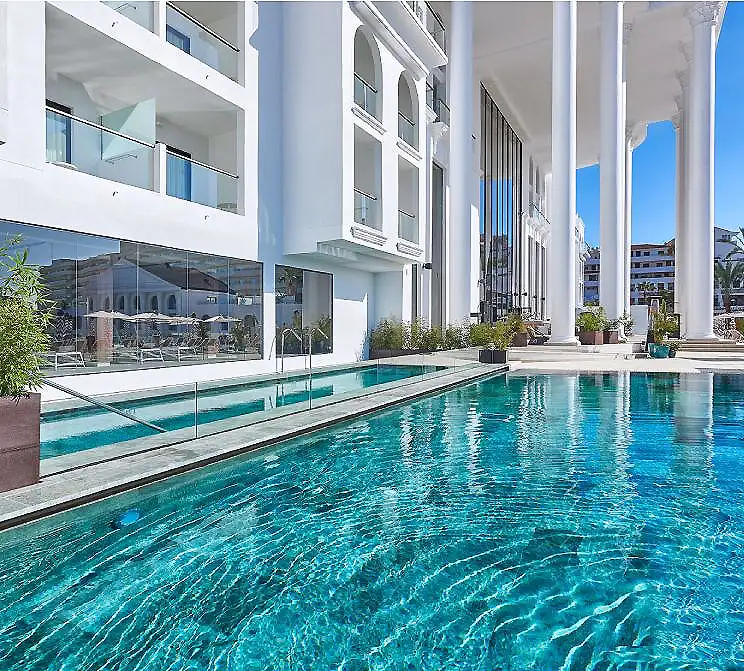 Piscina de hotel moderna con columnas y edificios blancos al fondo
