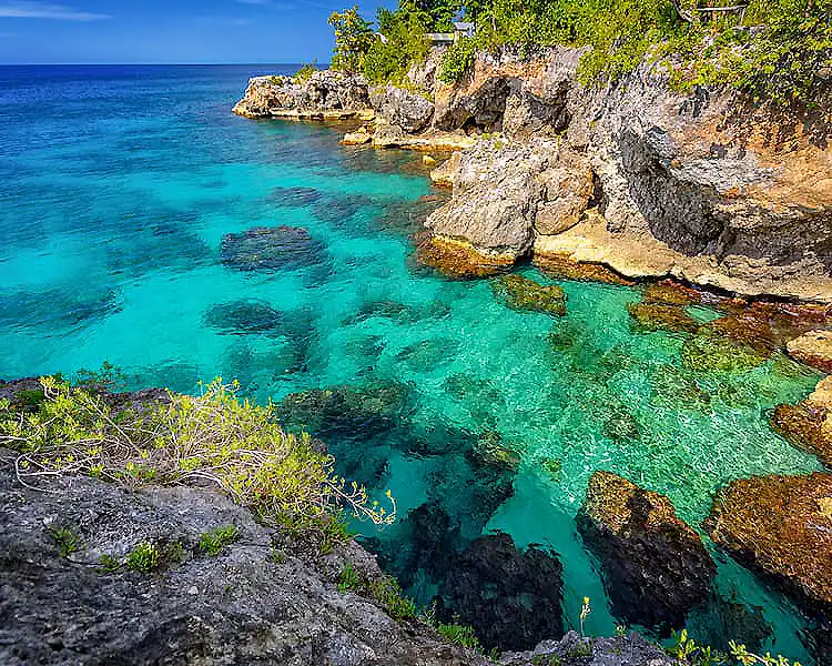 Acantilado de roca con aguas turquesa en la costa caribe&ntilde;a, vegetaci&oacute;n verde.