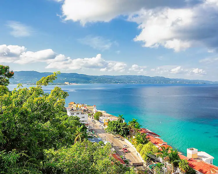 Vista panor&aacute;mica de costa con casas y agua turquesa bajo cielo nublado