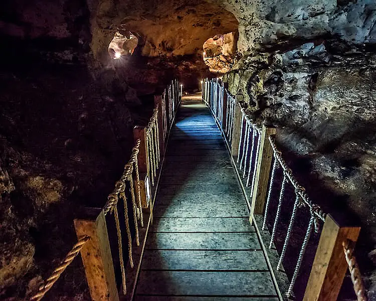 Pasarela colgante iluminada en una cueva oscura, entre rocas y cadenas