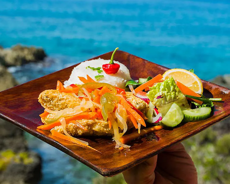 Plato de comida con ensalada, lim&oacute;n y cereza sobre tabla de madera, junto al mar