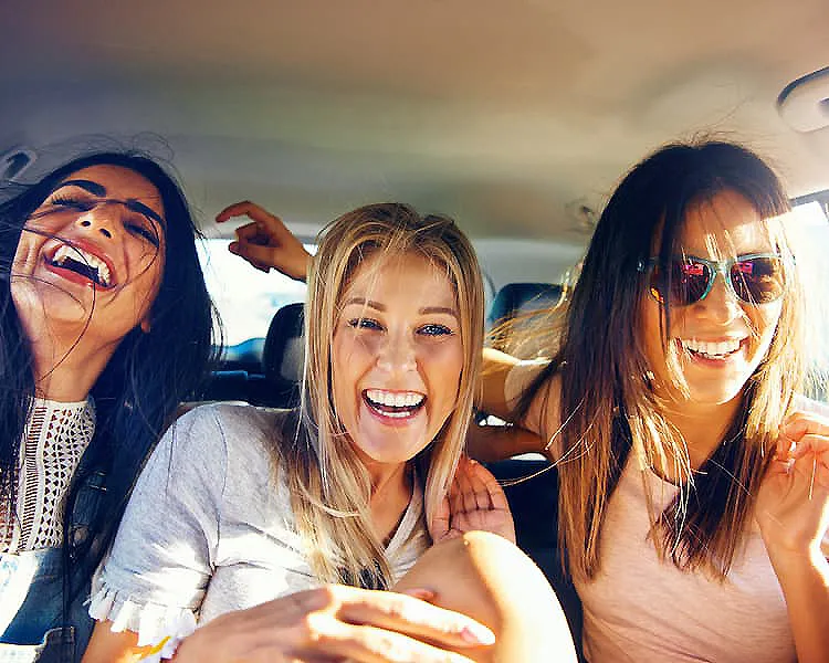 Tres amigas sonrientes en el coche, posando y riendo.