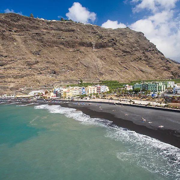 Playa con oleaje y edificios junto a un acantilado bajo el cielo nublado