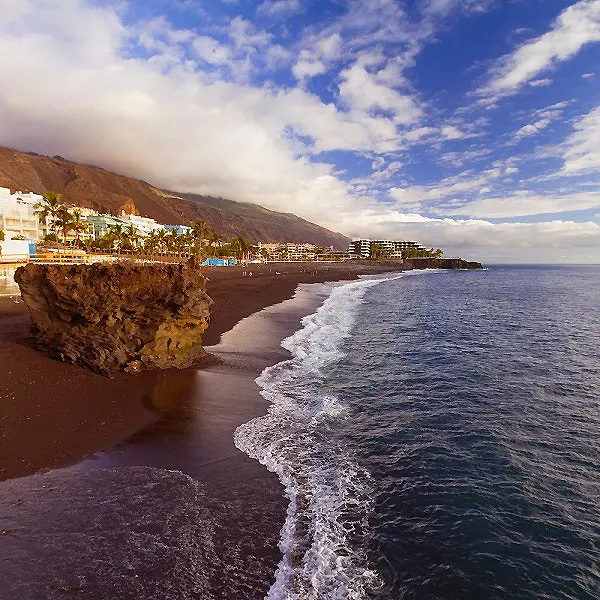Playa con acantilado, olas del oc&eacute;ano y cielo con nubes, costa de verano