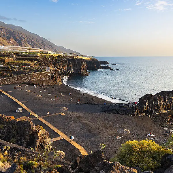 Playa con acantilados y camino costero, gente y mar al atardecer