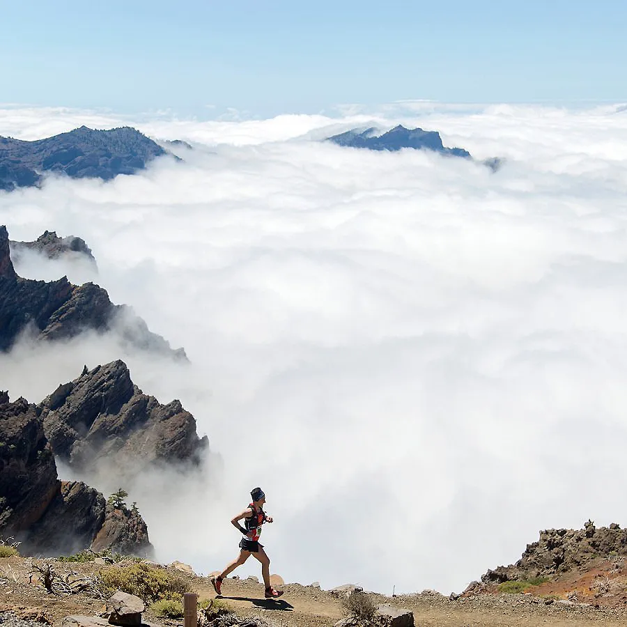 Senderista corriendo sobre rocas entre monta&ntilde;as y nubes de niebla
