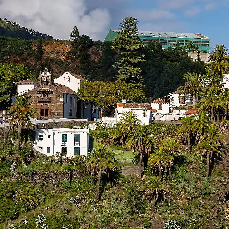 Pueblo costero con palmeras y casas blancas bajo cielo nublado y un edificio verde
