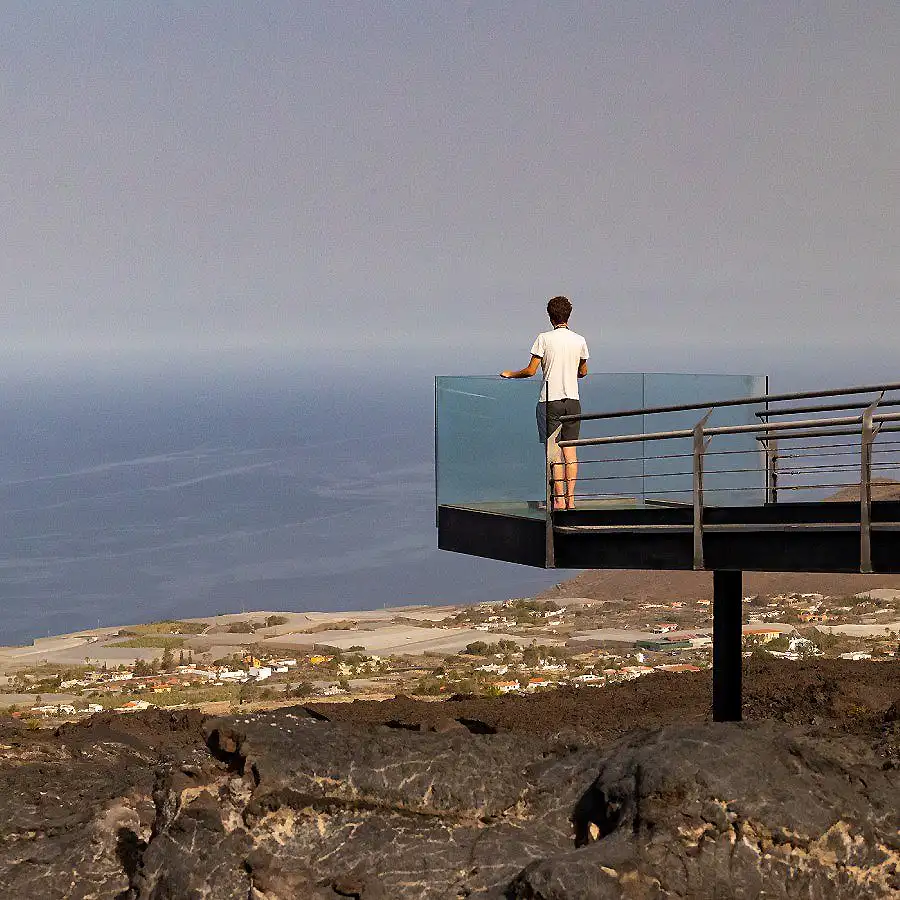 Persona de espaldas en una plataforma mirando el paisaje costero desde un mirador