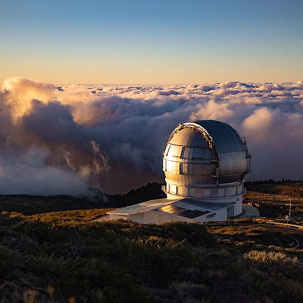 Telescopio en una c&uacute;pula sobre monta&ntilde;as con nubes al atardecer