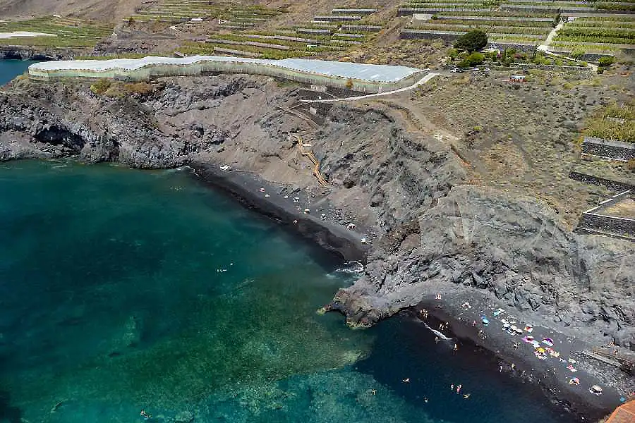 Playa y mar turquesa junto a un valle con terrazas agr&iacute;colas.