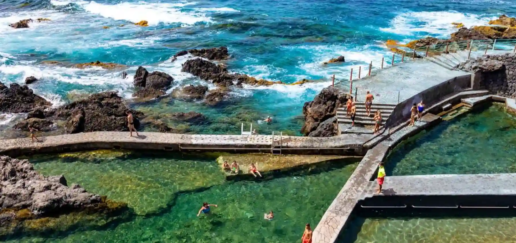 Personas nadan en una playa rocosa con escaleras y olas del oc&eacute;ano