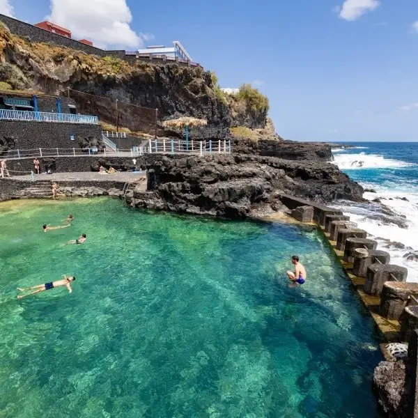 Piscina natural de roca con ba&ntilde;istas y acantilados junto al mar.