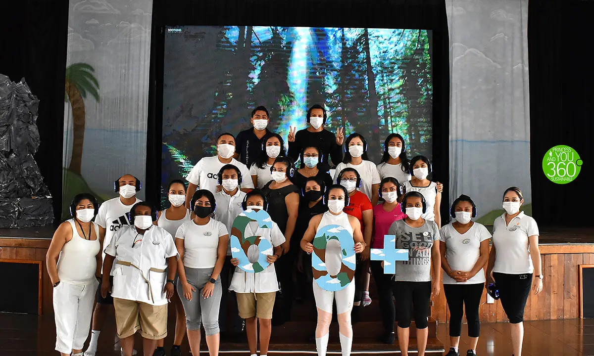 Equipo de personas con mascarillas y camisetas, posando ante un escenario con pantalla